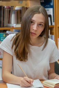 Teenage girl writing on book in library