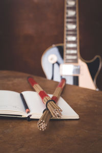 Notebook and drumsticks on table with guitar in background