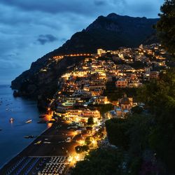 High angle view of illuminated city by sea against sky