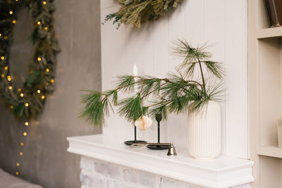 Spruce or pine branches in a white vase and candles in candlesticks on a shelf in a cozy room