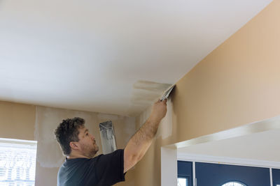 Rear view of man standing against wall at home