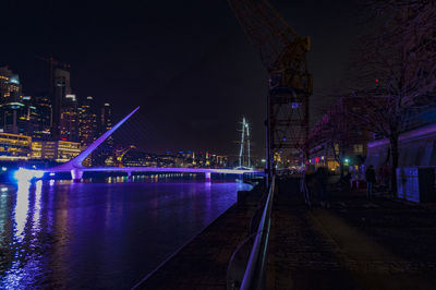 Illuminated bridge over river amidst buildings in city at night