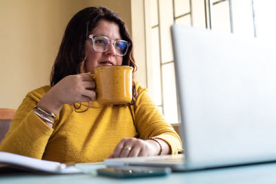 Smiling woman holding coffee cup looking at laptop at office