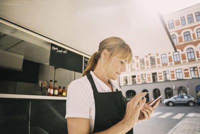 Close-up of female chef using mobile phone by food truck at city street