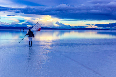 Rear view of man holding fishing net while walking at salar de uyuni against sky during sunset