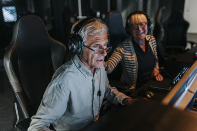 Elderly man with headset playing video game by female friend at gaming center