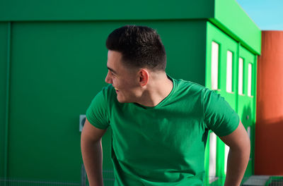 Young man looking away while standing against wall