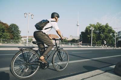 Businessman wearing helmet riding bicycle on road in city against sky