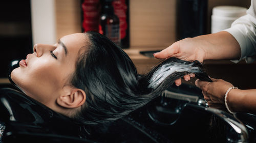 Cropped hands of hairdresser applying shampoo on woman hair in salon