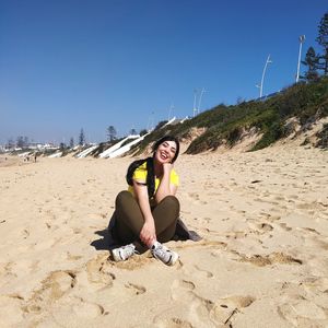 Portrait of young woman sitting on land against clear sky