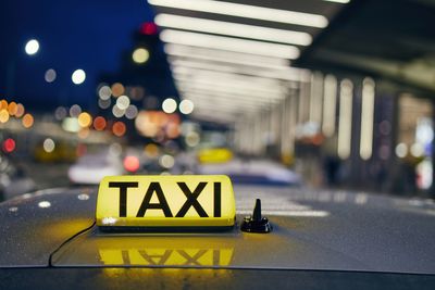 Lighting taxi sign on the roof of car against airport terminal at night.