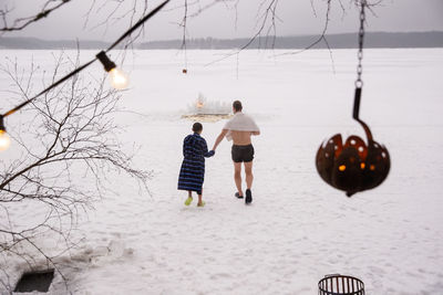 Rear view of father and son holding hands while walking on snow at frozen lake