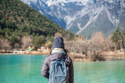 Rear view of woman standing by lake against mountains