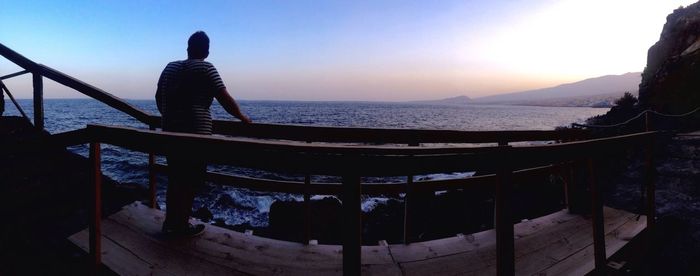 Rear view of silhouette man standing on railing against sea