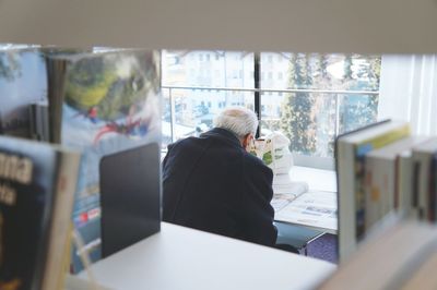 Rear view of senior man reading newspaper while sitting in library