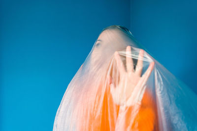 Woman covered in plastic standing against blue background