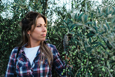 Young woman looking away while standing against plants