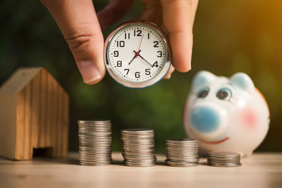 Close-up of hand holding clock over coins and model house on table