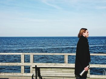 Side view of mid adult man standing on pier by sea