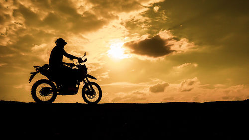 Silhouette woman riding bicycle on field against sky during sunset