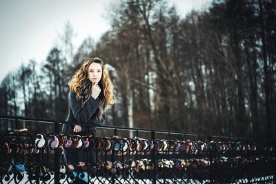 Portrait of woman standing by railing against trees