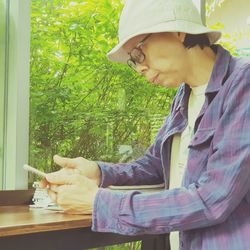 Side view of mature woman using mobile phone while sitting by window