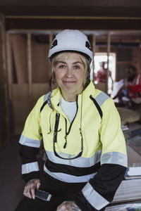 Smiling female building contractor wearing hard hat sitting at construction site