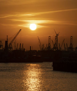 Silhouette cranes at commercial dock against sky during sunset