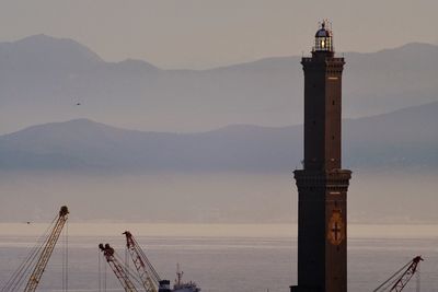 Lighthouse by sea against sky during sunset