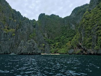 Scenic view of sea by mountain against sky