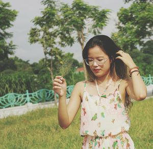 Young woman standing on field against trees