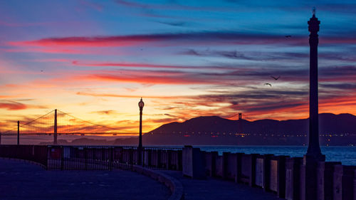 Silhouette street by sea against orange sky