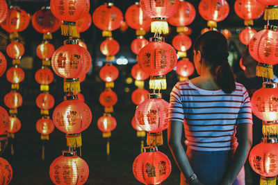 Rear view of woman standing against illuminated red lanterns hanging at night