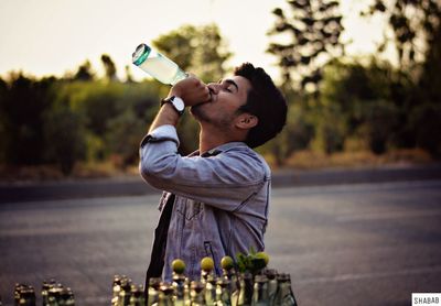 Side view of young man drinking drink from bottle on street