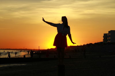 Silhouette woman on beach against sky during sunset