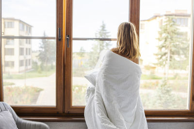 Rear view of woman looking through window at home