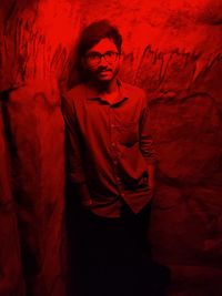 Portrait of young man standing against red wall