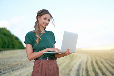 Young woman using phone while standing on field