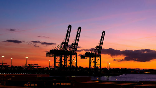 Silhouette cranes at pier against sky during sunset