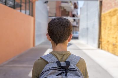 Rear view of teenage boy with backpack standing outdoors