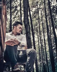 Young man looking down while sitting on tree trunk