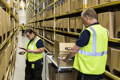 Coworkers working on aisle amidst racks at distribution warehouse