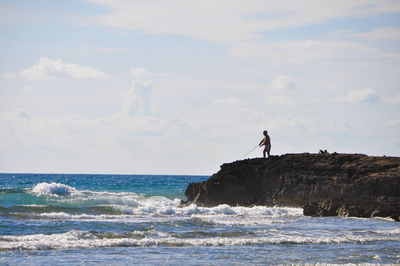 Man on rock by sea against sky