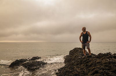 Full length of man standing on rock at sea shore against sky