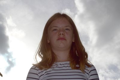 Low angle view of thoughtful girl standing against cloudy sky