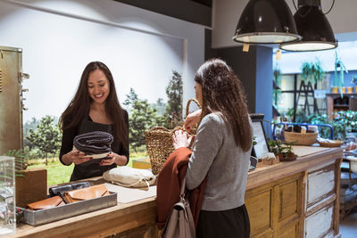 Saleswoman selling merchandise to female customer at checkout counter