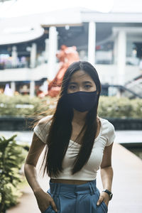 Portrait of young woman standing against building