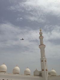 Low angle view of mosque and airplane against cloudy sky on sunny day