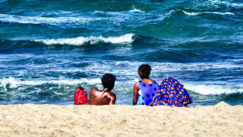 Rear view of men and woman sitting on shore at beach