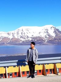 Full length of woman standing on snowcapped mountain against blue sky